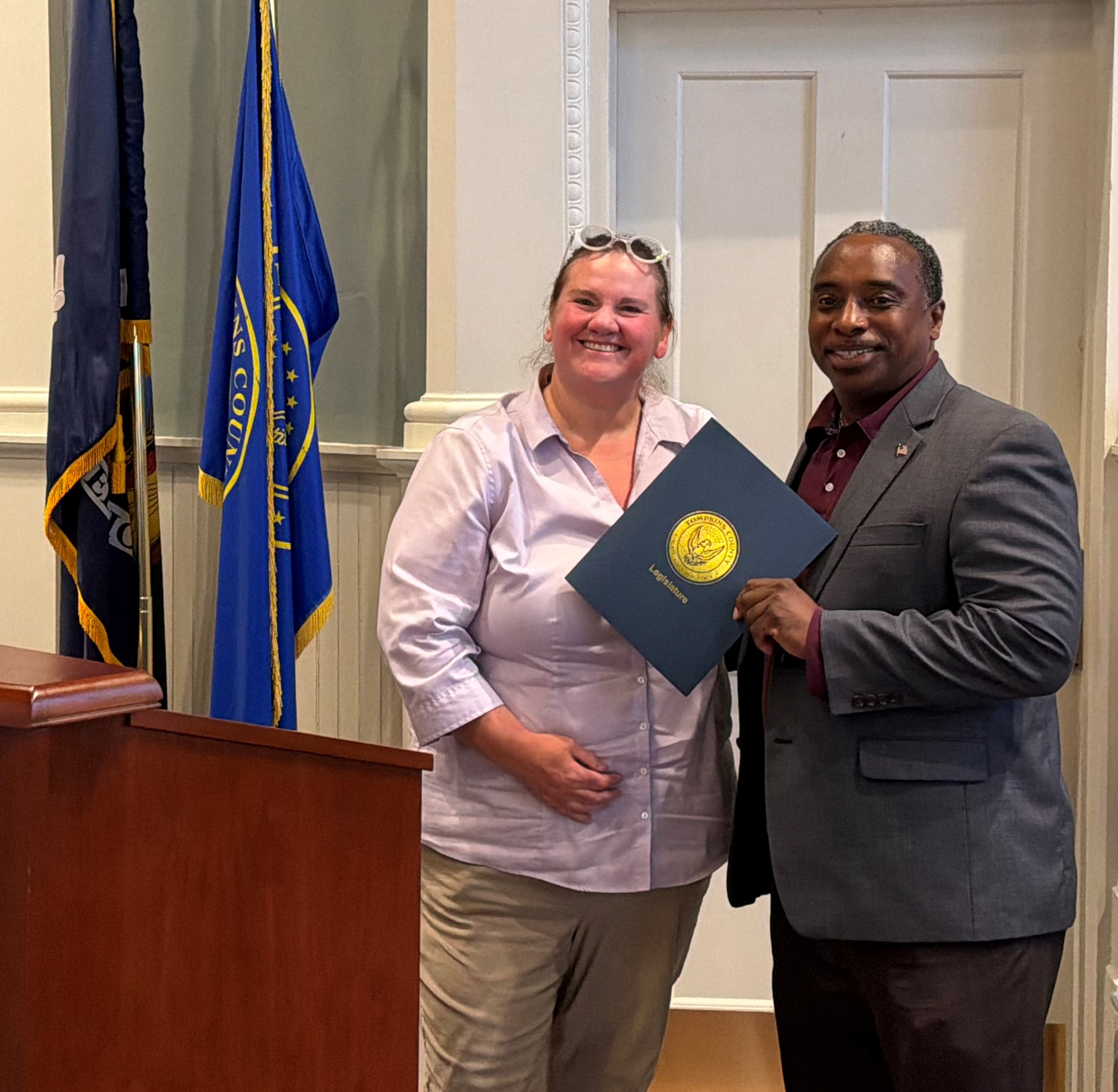 Chair of the Legislature presents proclamation to Veterans Services Director standing in front of flags and behind a podium