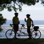 photo of silhouettes of  two cyclists standing by bikes in front of the lake
